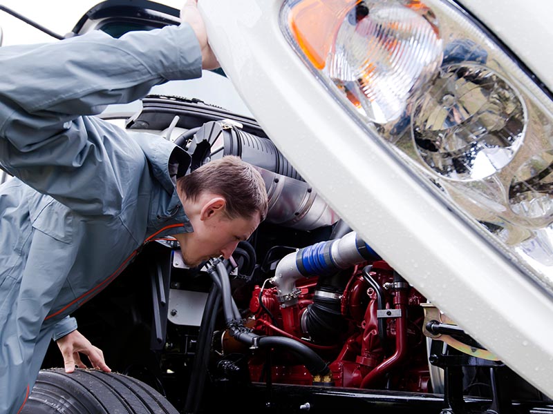 man inspecting large truck engine