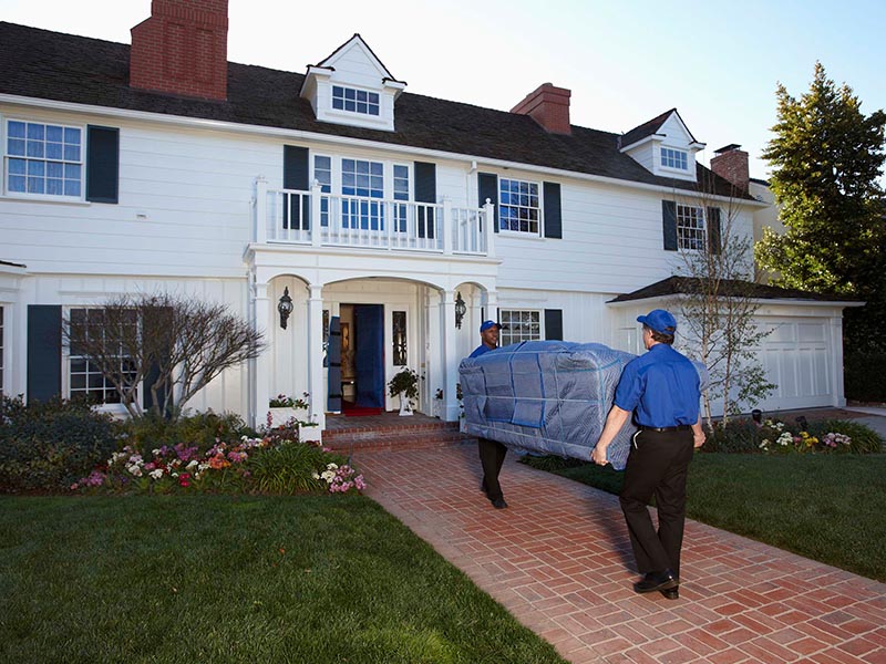 home movers carrying wrapped couch into home