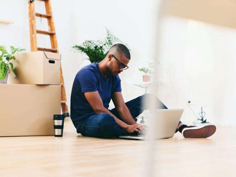 man sitting on floor with laptop and moving boxes